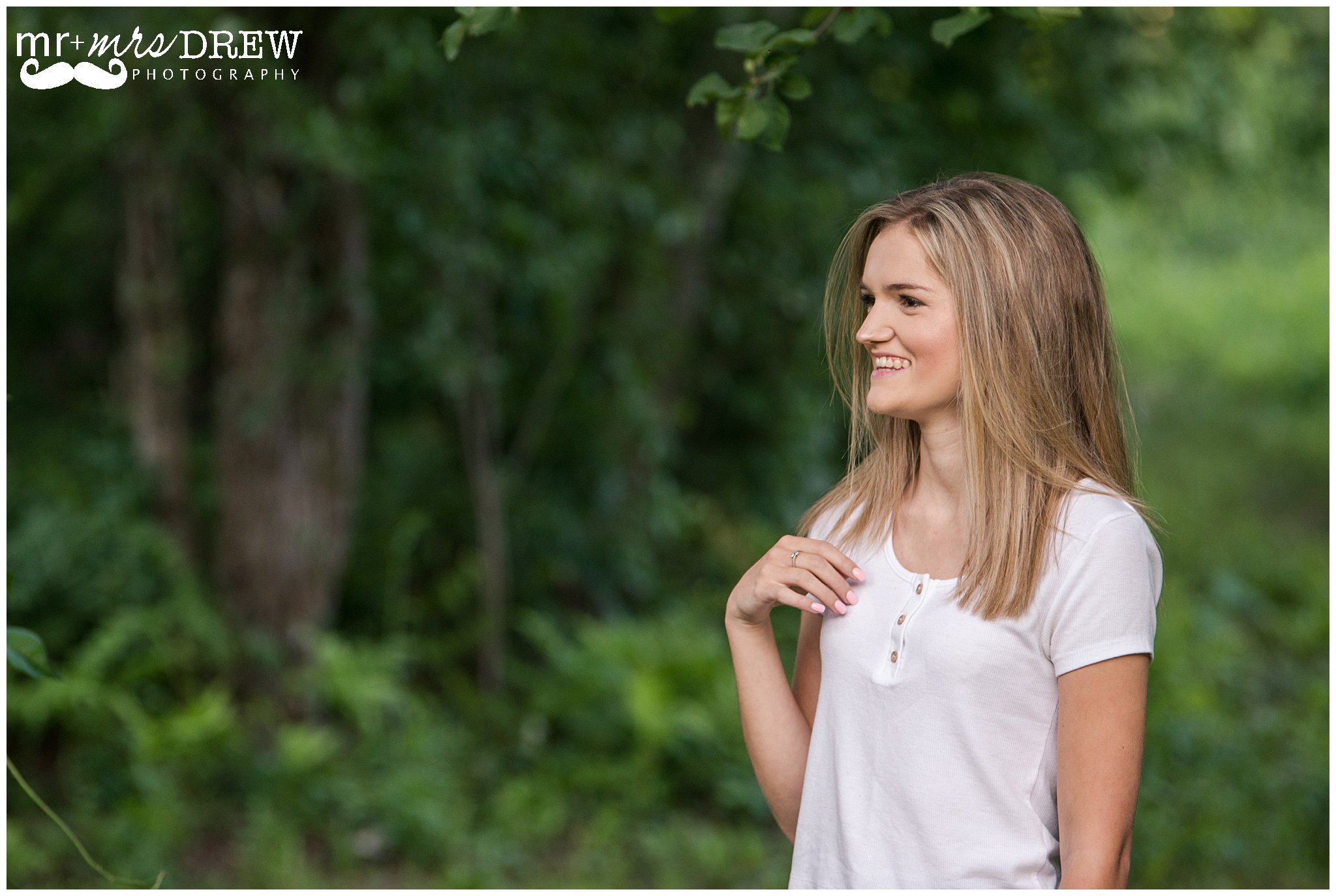 Senior Portrait of girl in white t-shirt playing with her hair looking to the side. 