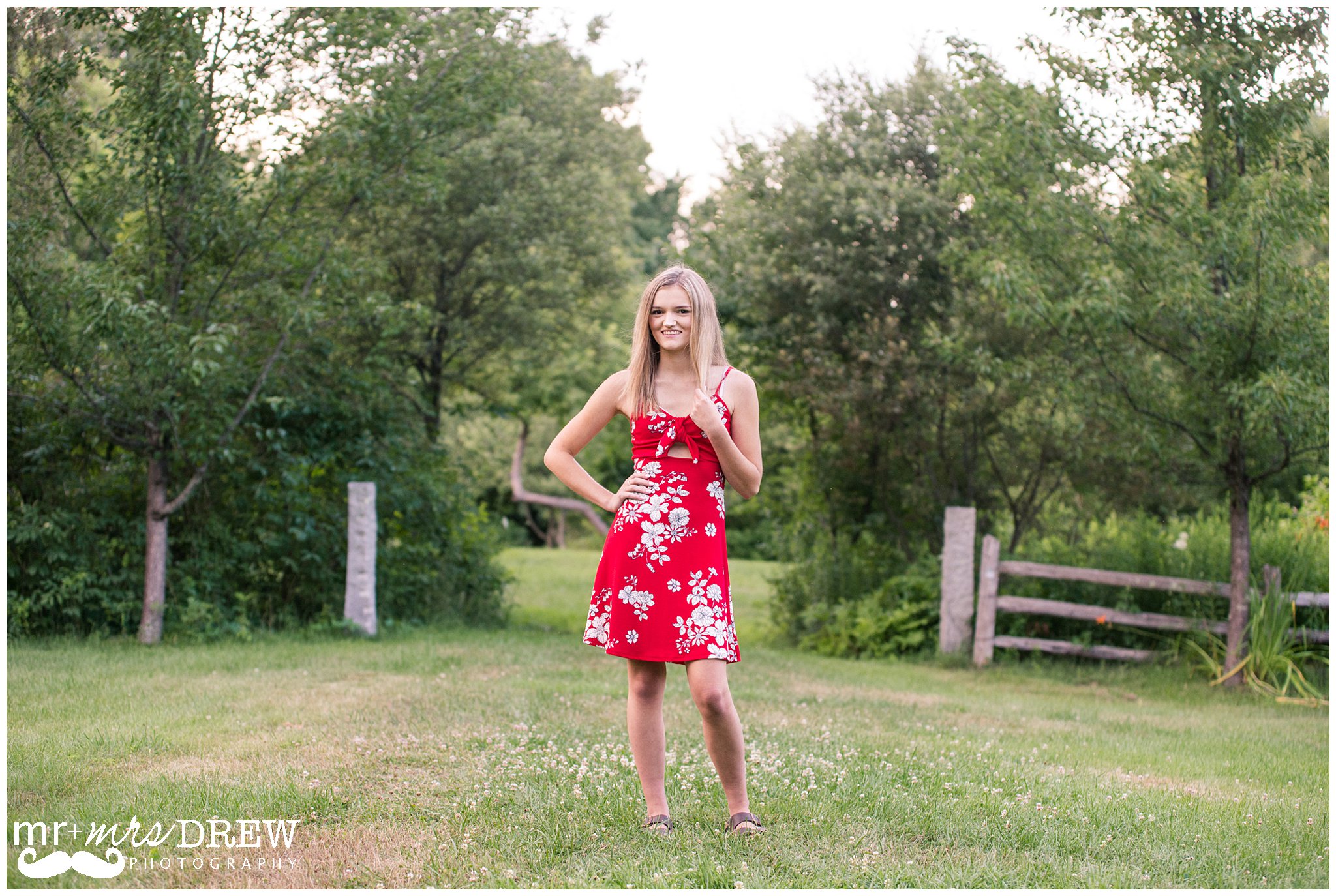 Senior Portrait of girl in Red floral dress hand on her hip and playing with her hair. 