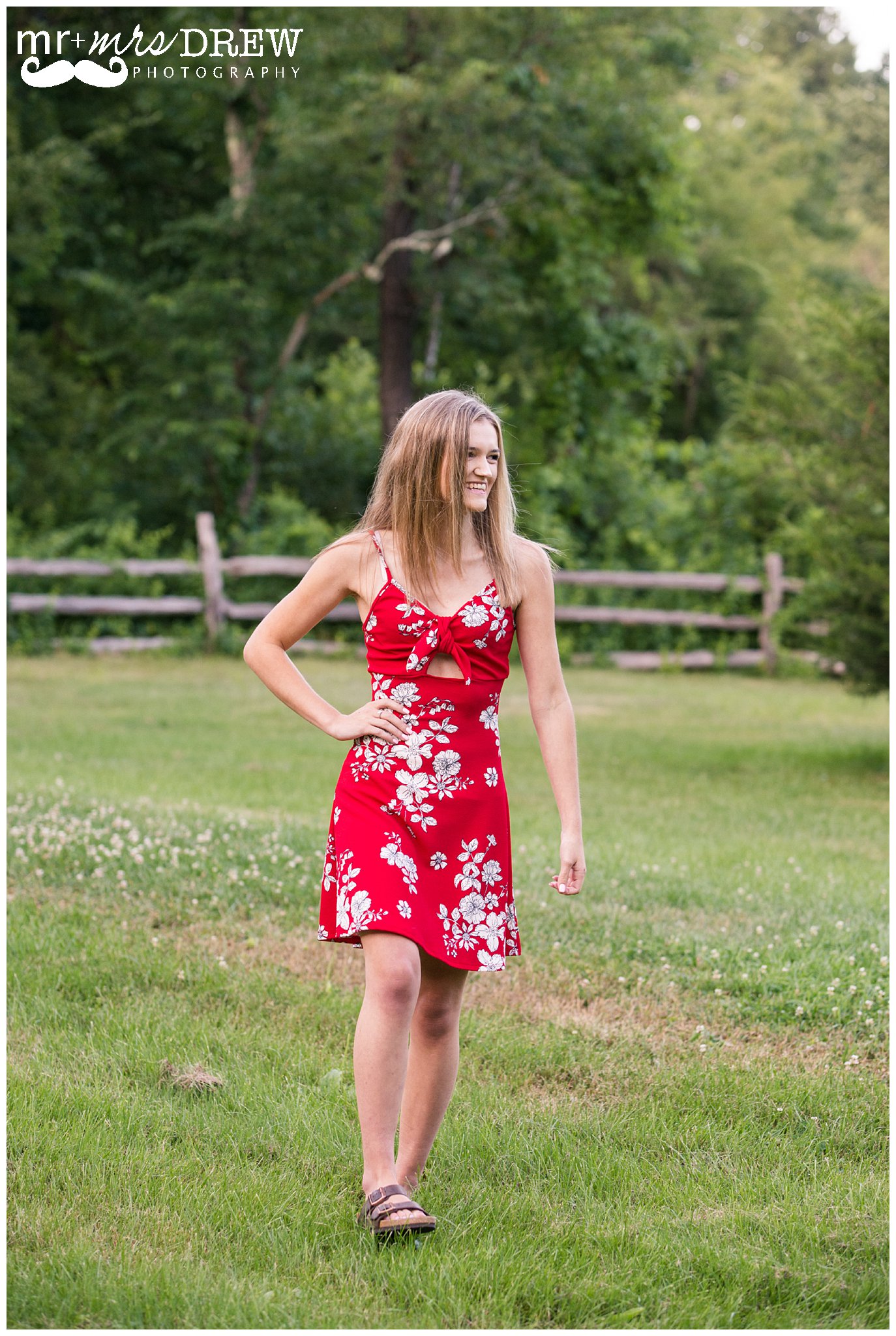 Senior Portrait of girl in Red floral dress walking while looking to the side. 