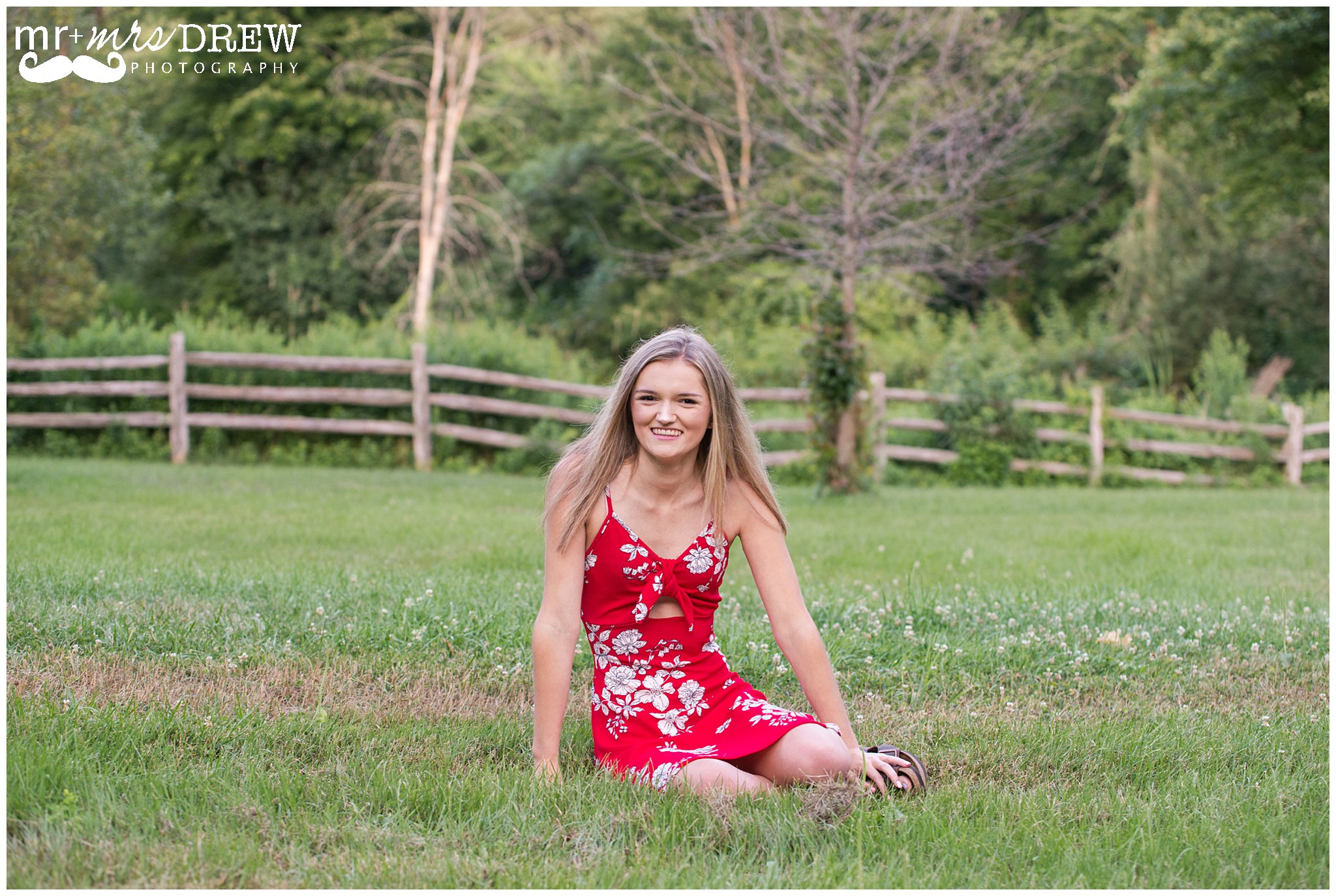 Senior Portrait of girl in Red floral dress sitting in the grass. 