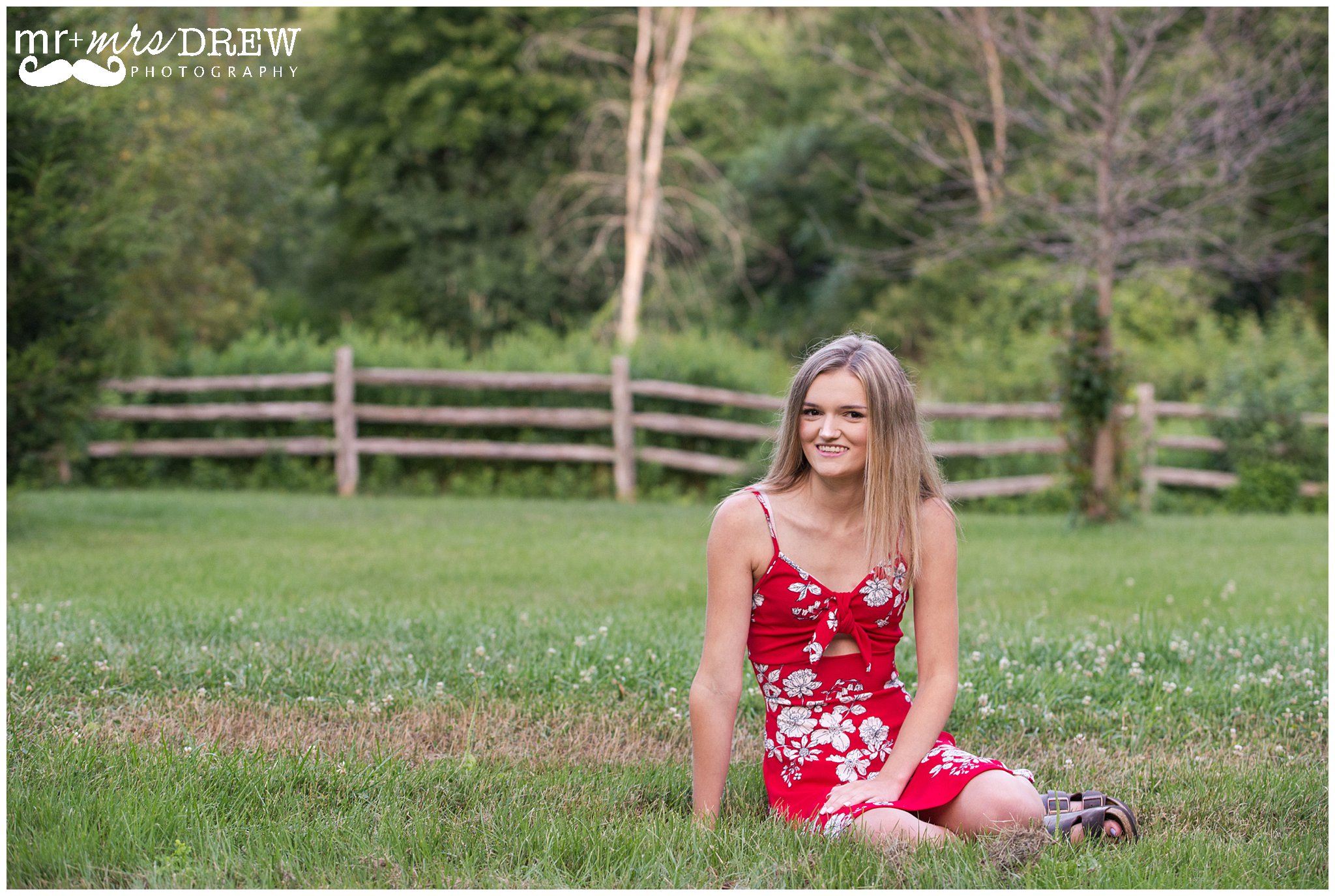 Senior Portrait of girl in Red floral dress sitting in the grass. 