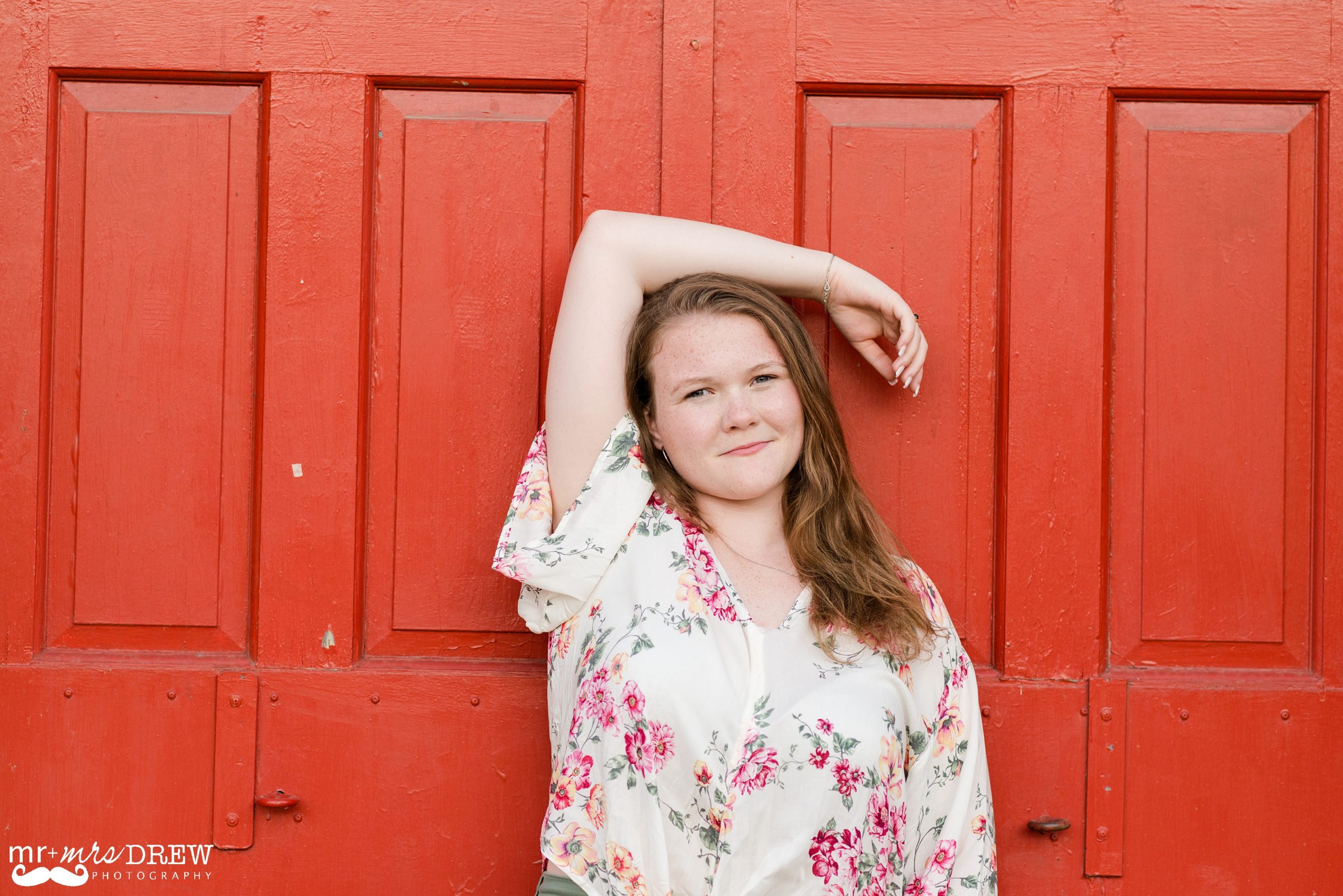 Senior Portraits Downtown Lowell - Meredyth is leaning against a red wall with her arm above her head.