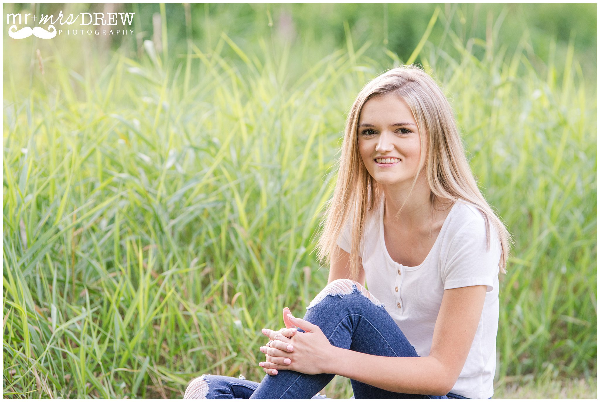 Senior Portrait of girl in white t-shirt & ripped jeans sitting in grass.
