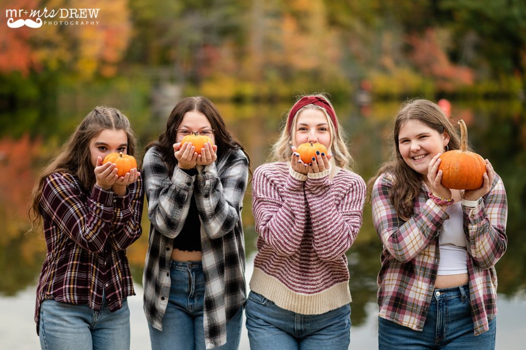 senior girls holding tiny pumpkins up to their faces at Heart Pond Chelmsford, MA
