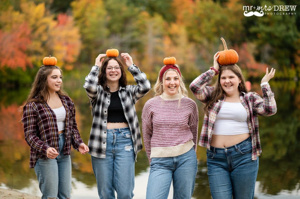 Senior girls balancing tiny pumpkins on their heads and smiling at Heart Pond Chelmsford MA