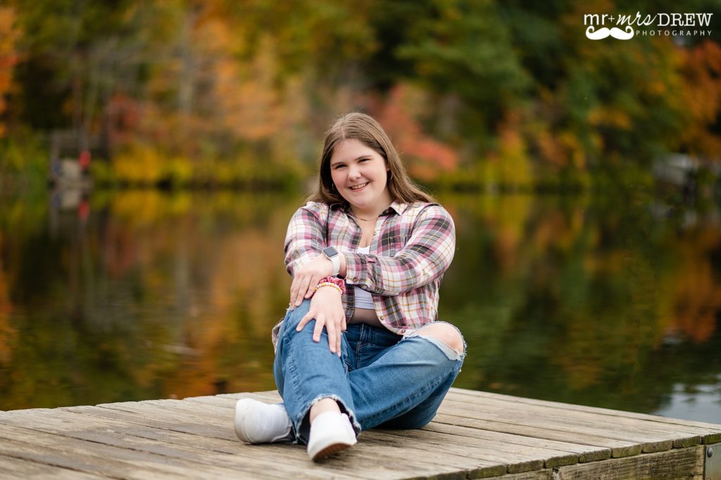 Chelmsford High senior sitting on dock with fall foliage reflecting in the water
